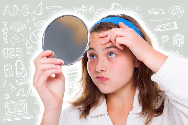 A school girl with a mirror, looking at a pimple on her forehead